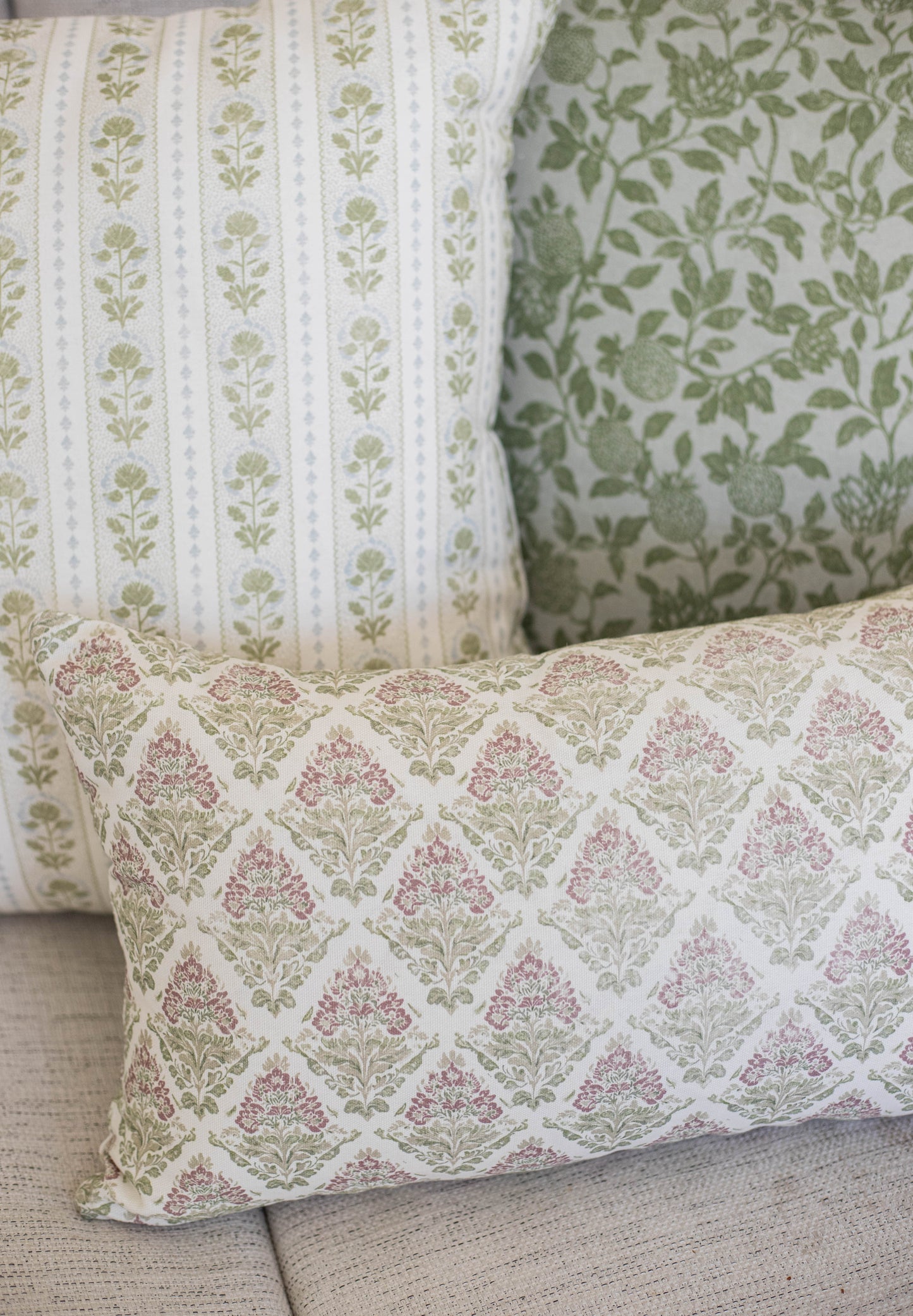 Five decorative pillows with botanical floral patterns in green, pink, and cream colors arranged on a gray sofa.
