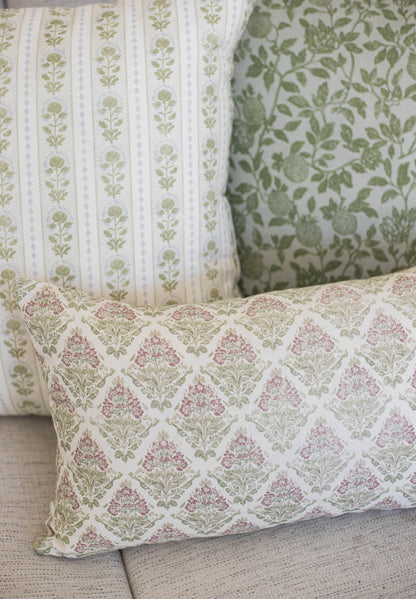 Five decorative pillows with botanical floral patterns in green, pink, and cream colors arranged on a gray sofa.