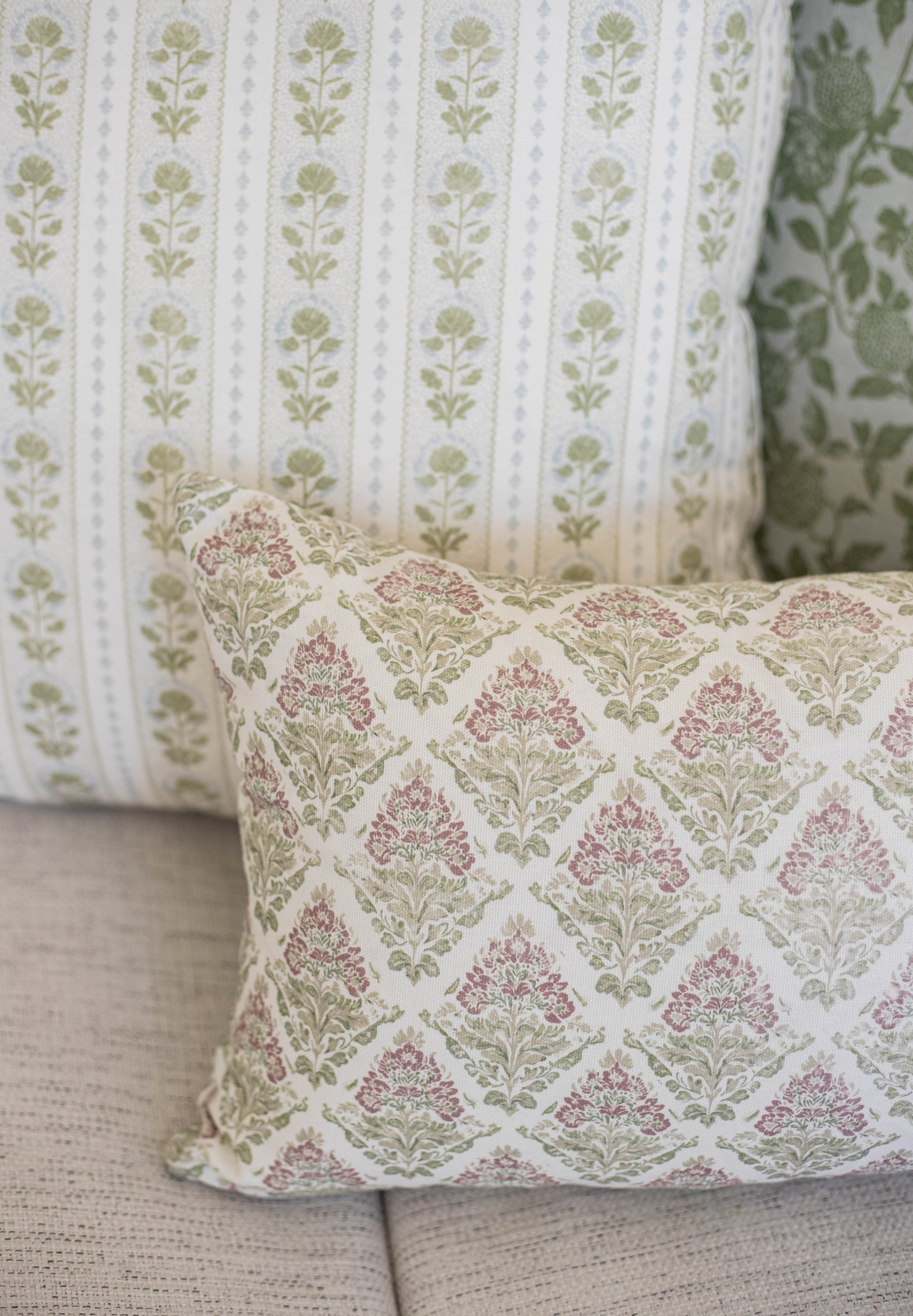 Five decorative pillows with floral damask and botanical stripe patterns in cream, mauve, and sage green.