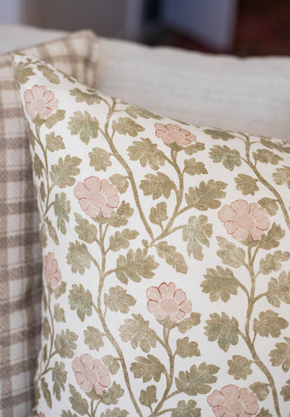 Decorative pillow with pink flowers and olive green leaves on cream background.