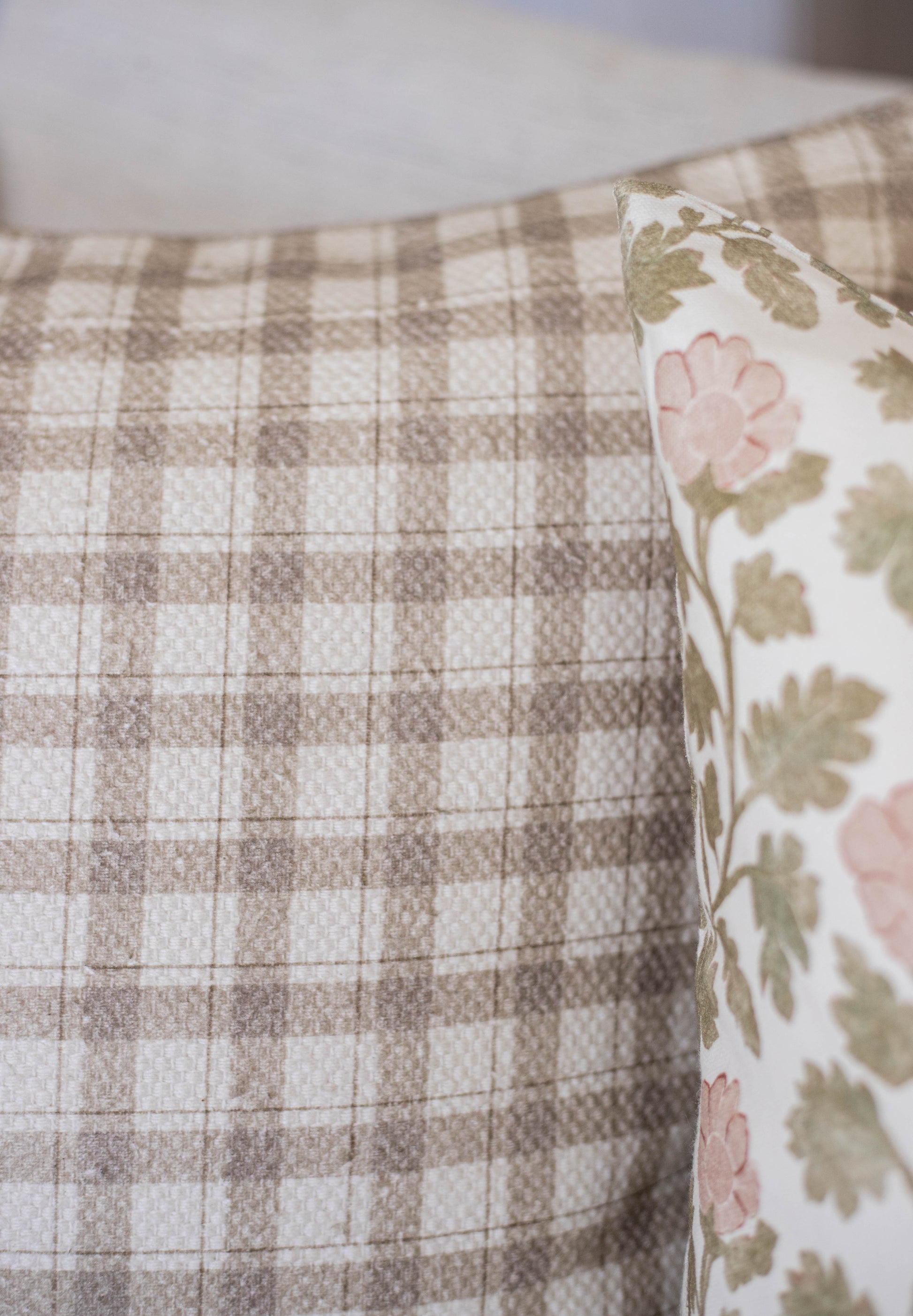Beige and white checked cotton fabric with a floral patterned pillow showing pink flowers and green leaves.