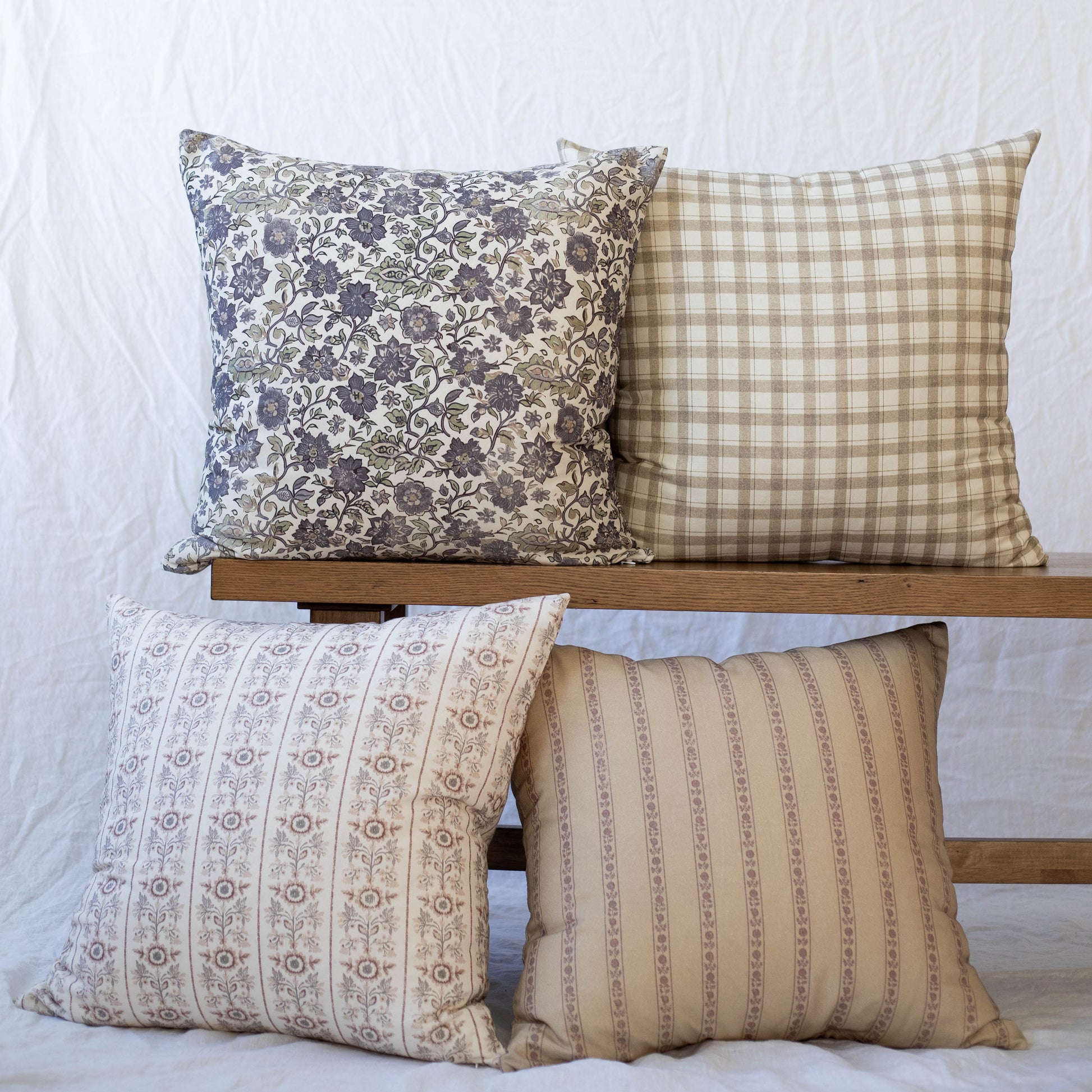 Four decorative pillows with floral, gingham, and striped patterns in navy, tan, and cream tones.