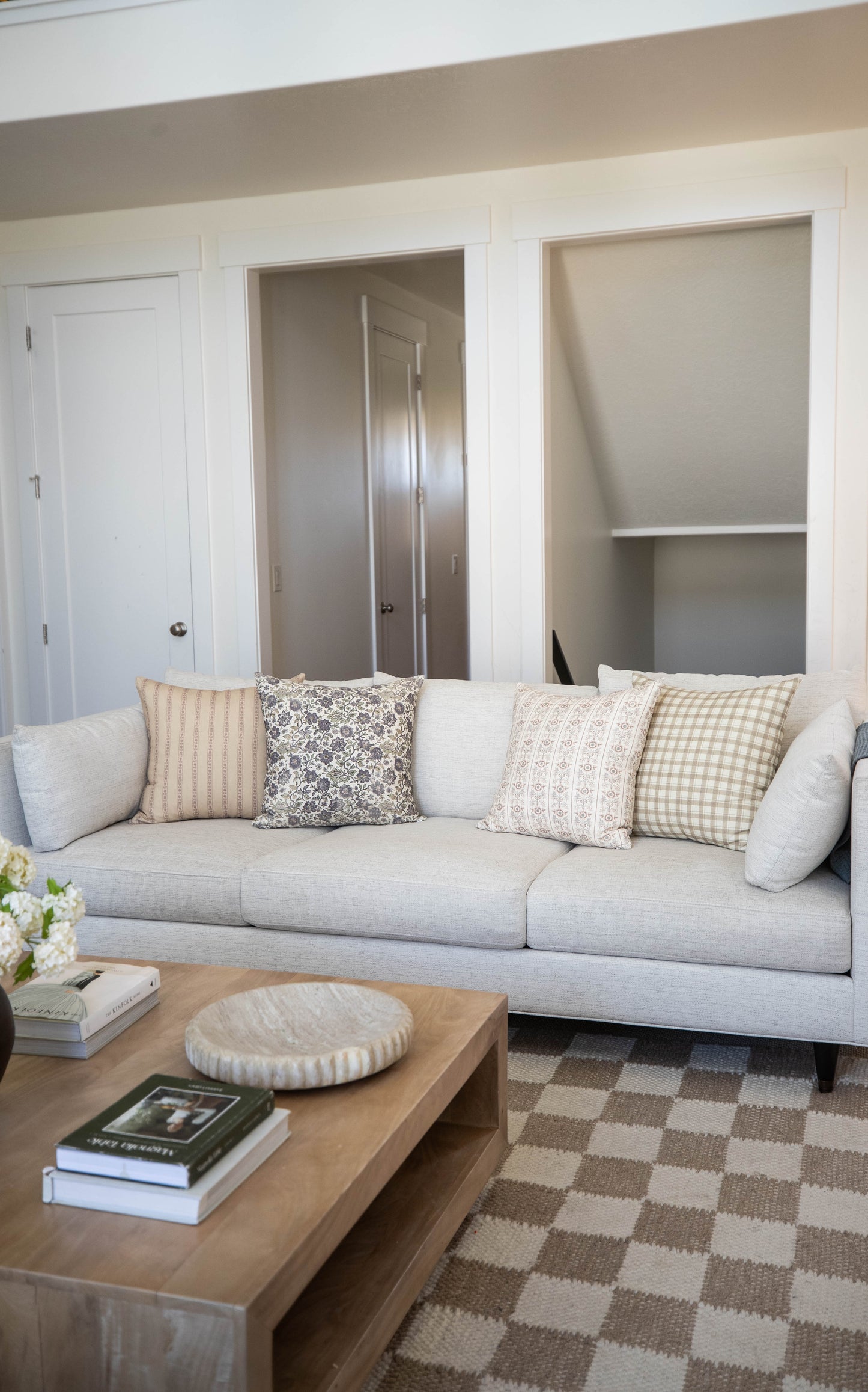 Four decorative throw pillows in neutral tones with striped, floral, solid, and checkered patterns displayed on a light gray 
