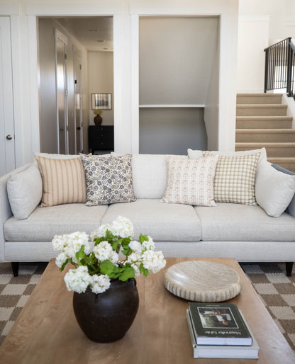 Four decorative pillows in neutral tones with striped, floral, and checkered patterns displayed on a light gray sofa.