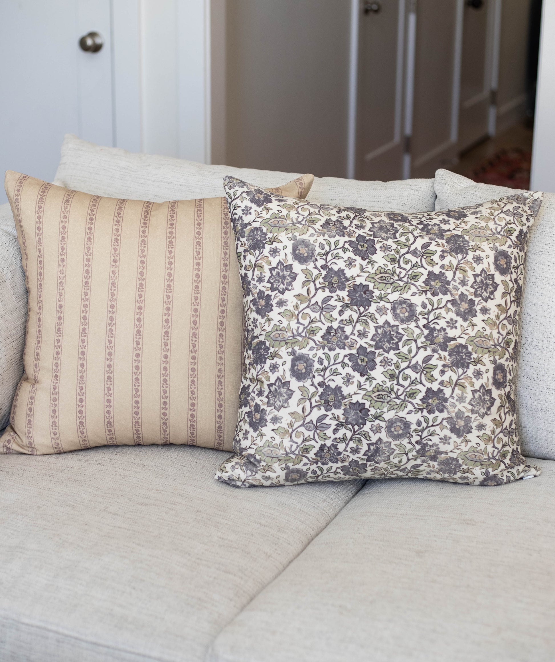 Two decorative pillows on a beige sofa: one with tan vertical stripes and one with blue floral damask pattern.