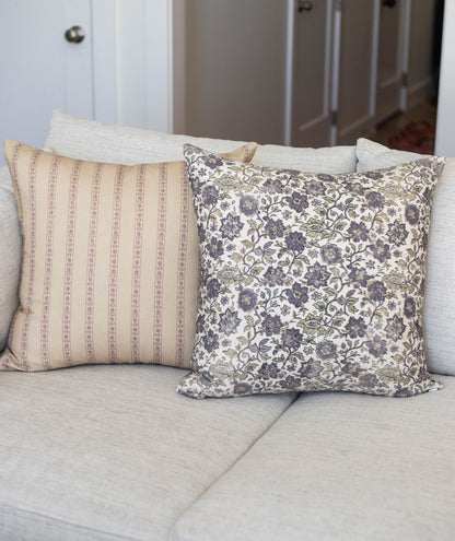 Two decorative pillows on a beige sofa: one with tan vertical stripes and one with blue floral damask pattern.