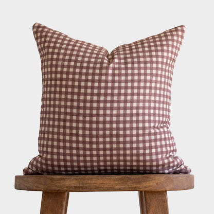 Rose-colored gingham patterned pillow with white checks displayed on a wooden stool.