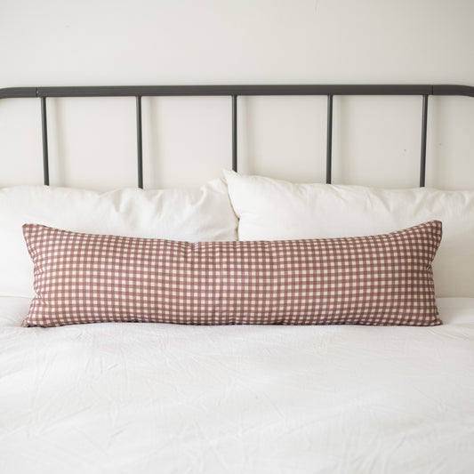 Rose and white gingham patterned lumbar pillow on a bed with white pillows and metal headboard.
