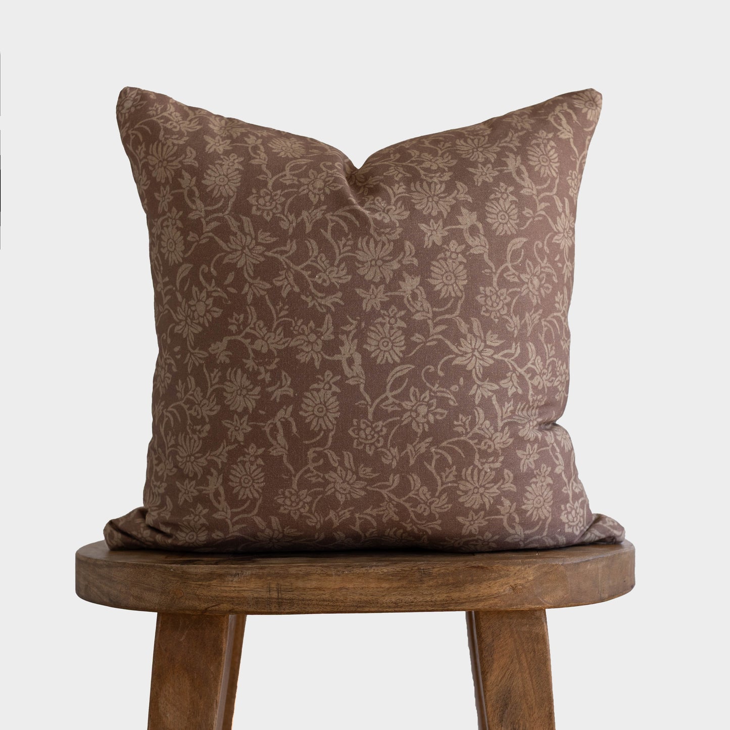 Brown damask patterned pillow with taupe floral design displayed on wooden stool.