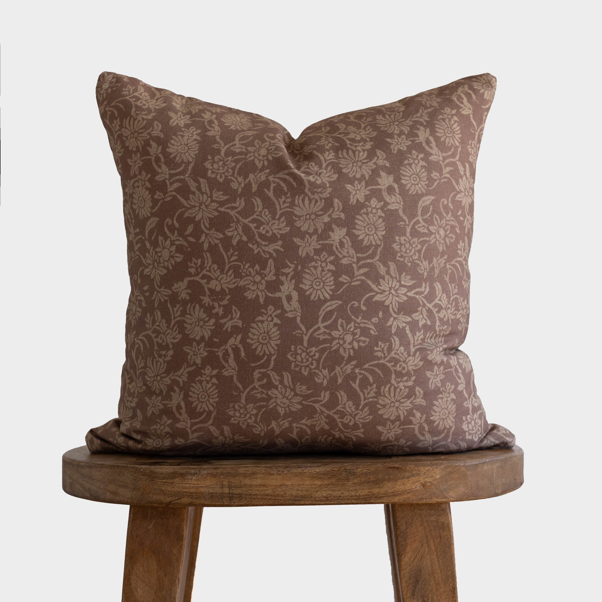 Brown damask patterned pillow with taupe floral design displayed on wooden stool.