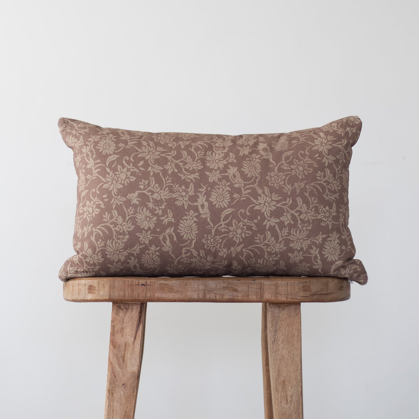 Brown damask patterned rectangular pillow with piping, displayed on a wooden stool.