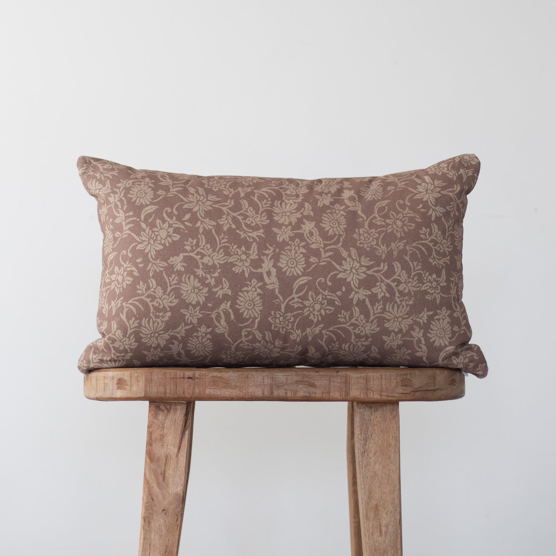 Brown damask patterned rectangular pillow with piping, displayed on a wooden stool.