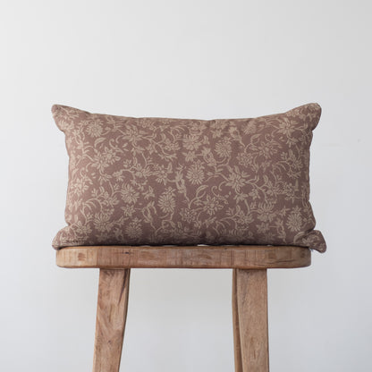 Brown damask patterned rectangular pillow with piping, displayed on a wooden stool.