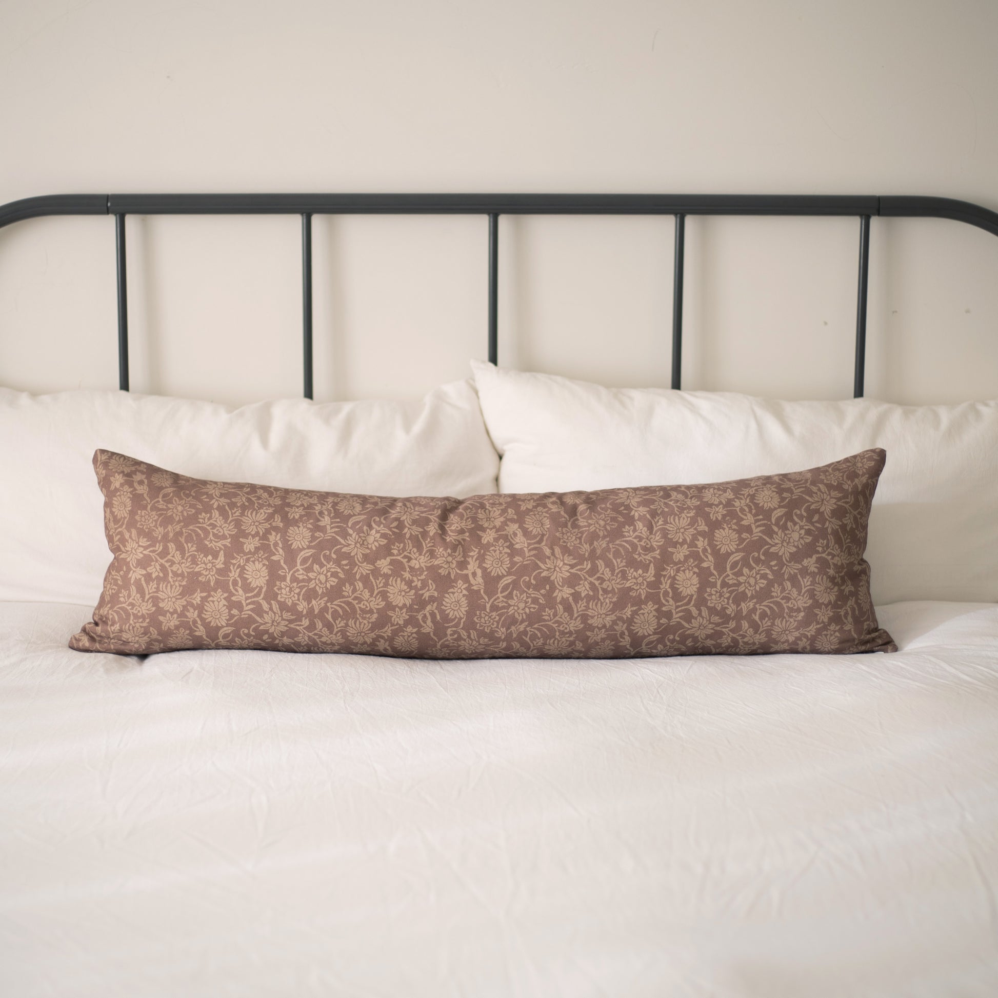 Brown patterned lumbar pillow on white bedding with black metal headboard.