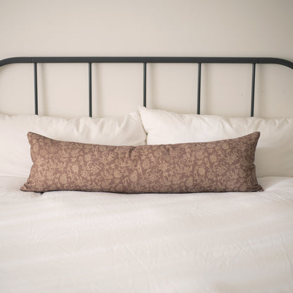 Brown patterned lumbar pillow on white bedding with black metal headboard.