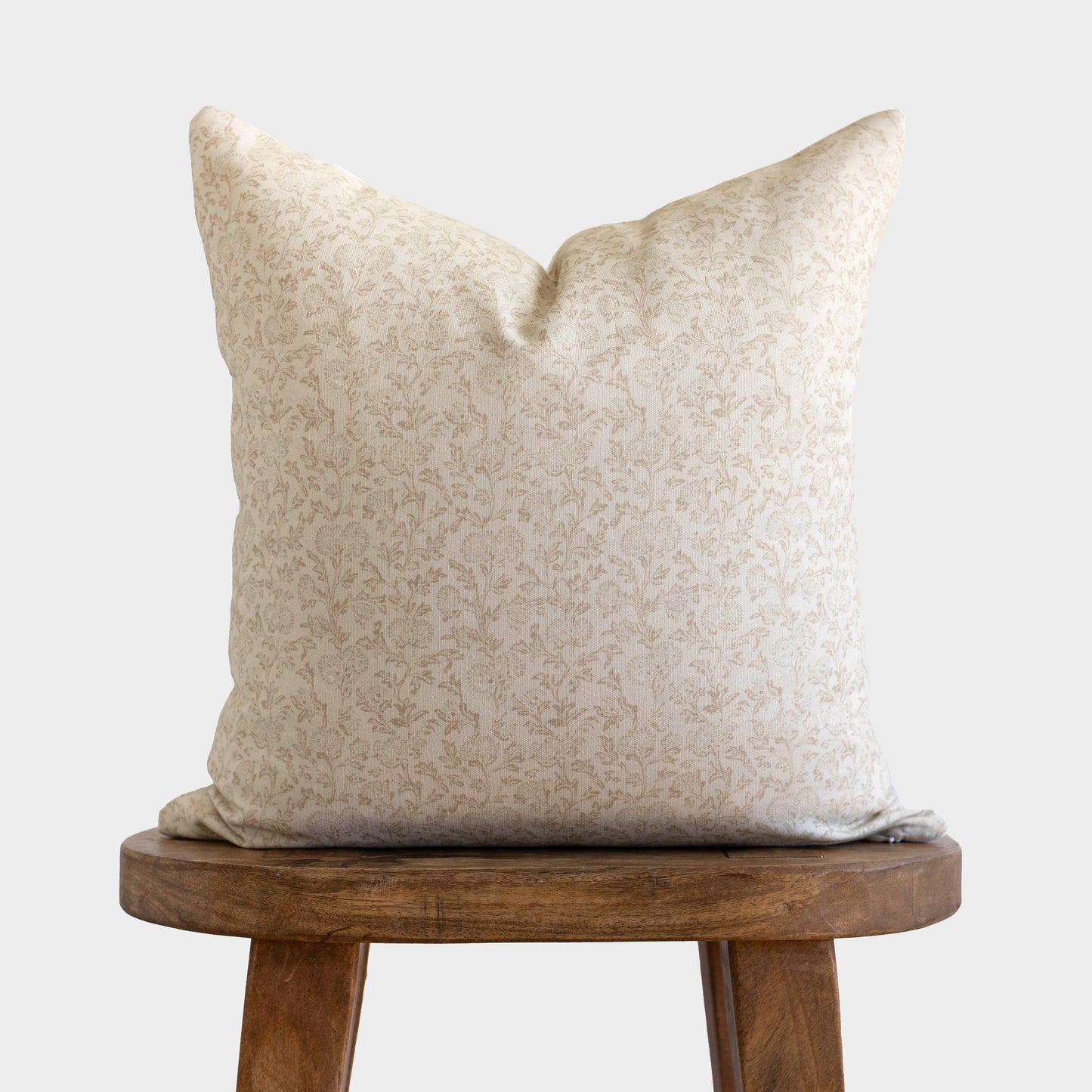 Cream pillow with subtle leaf pattern on wooden stool against white background.