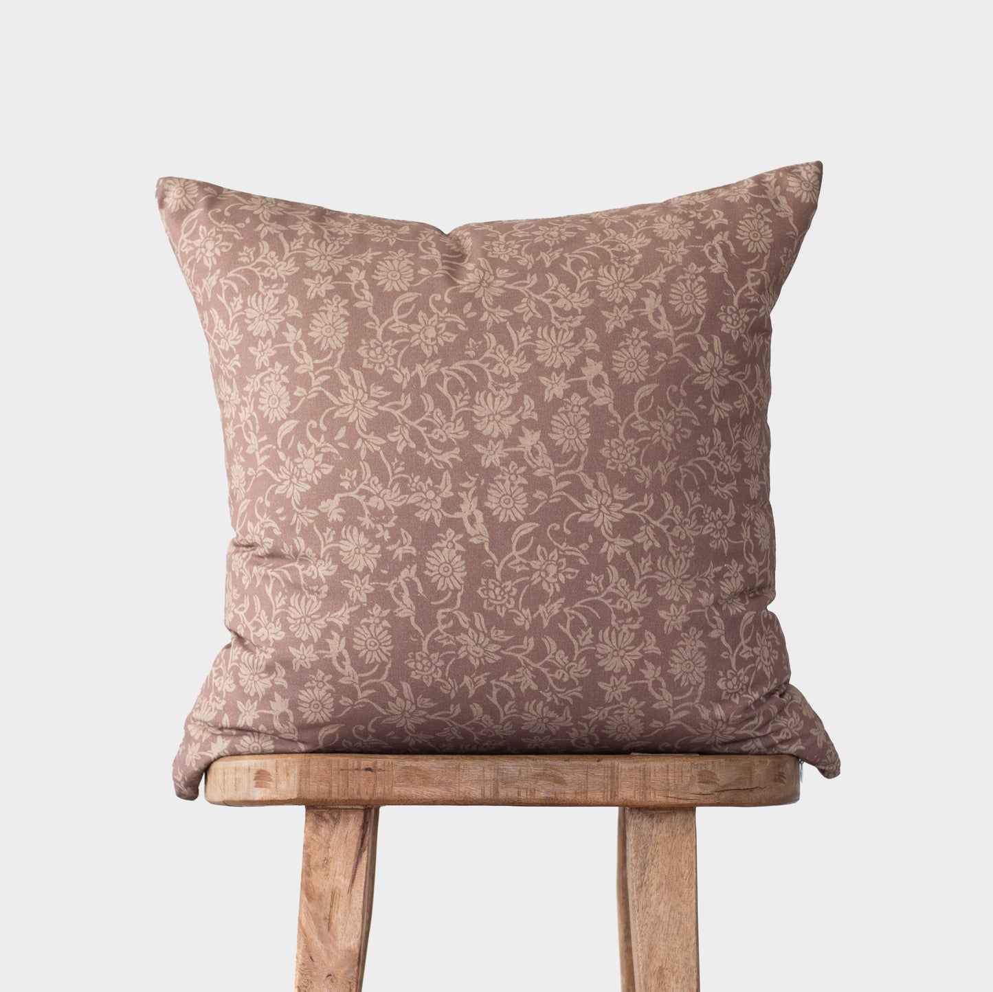 Taupe damask patterned pillow with cream floral motif displayed on wooden stool.