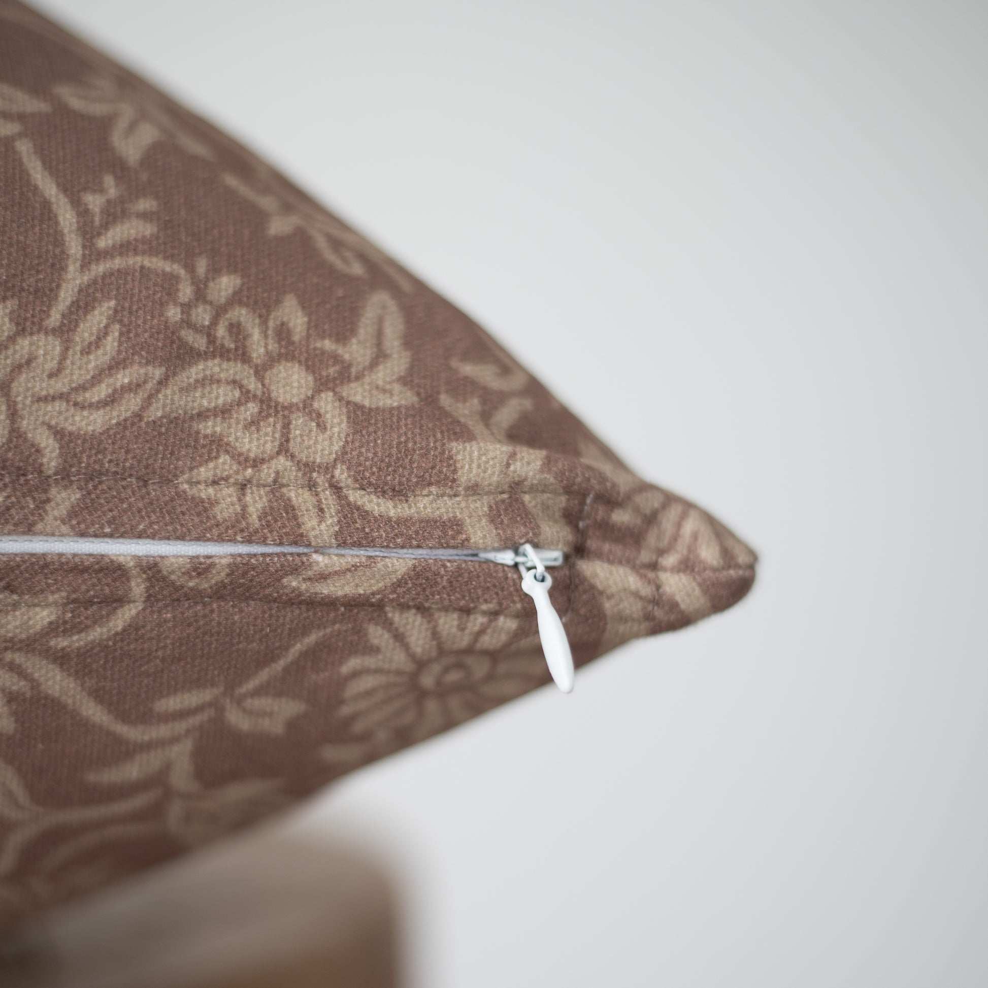Brown damask patterned pillow with white zipper closure and piping detail.