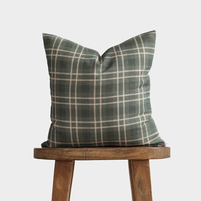 Green and white plaid cushion cover displayed on a wooden stool against a light background.