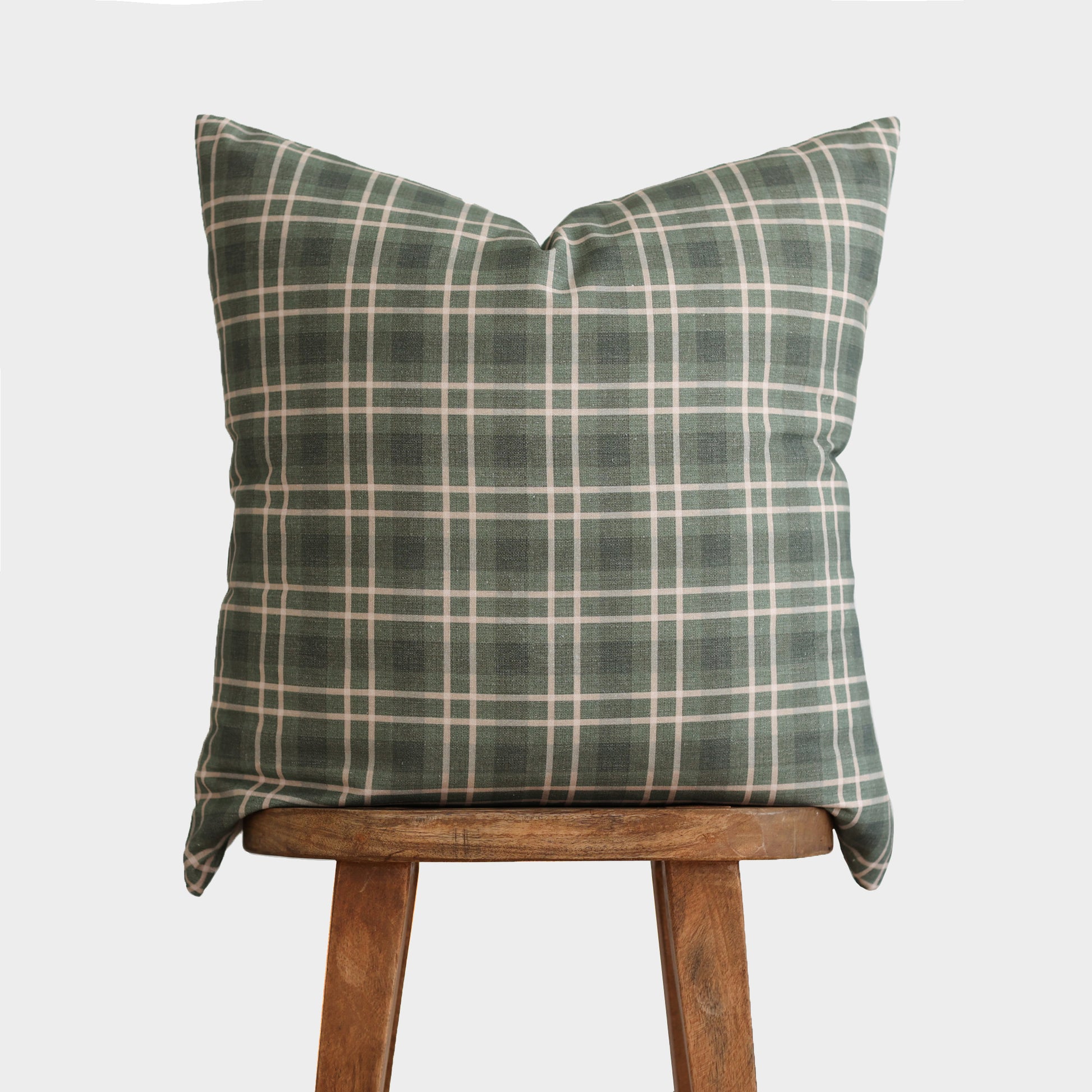 Green and cream plaid throw pillow displayed on a wooden stool.