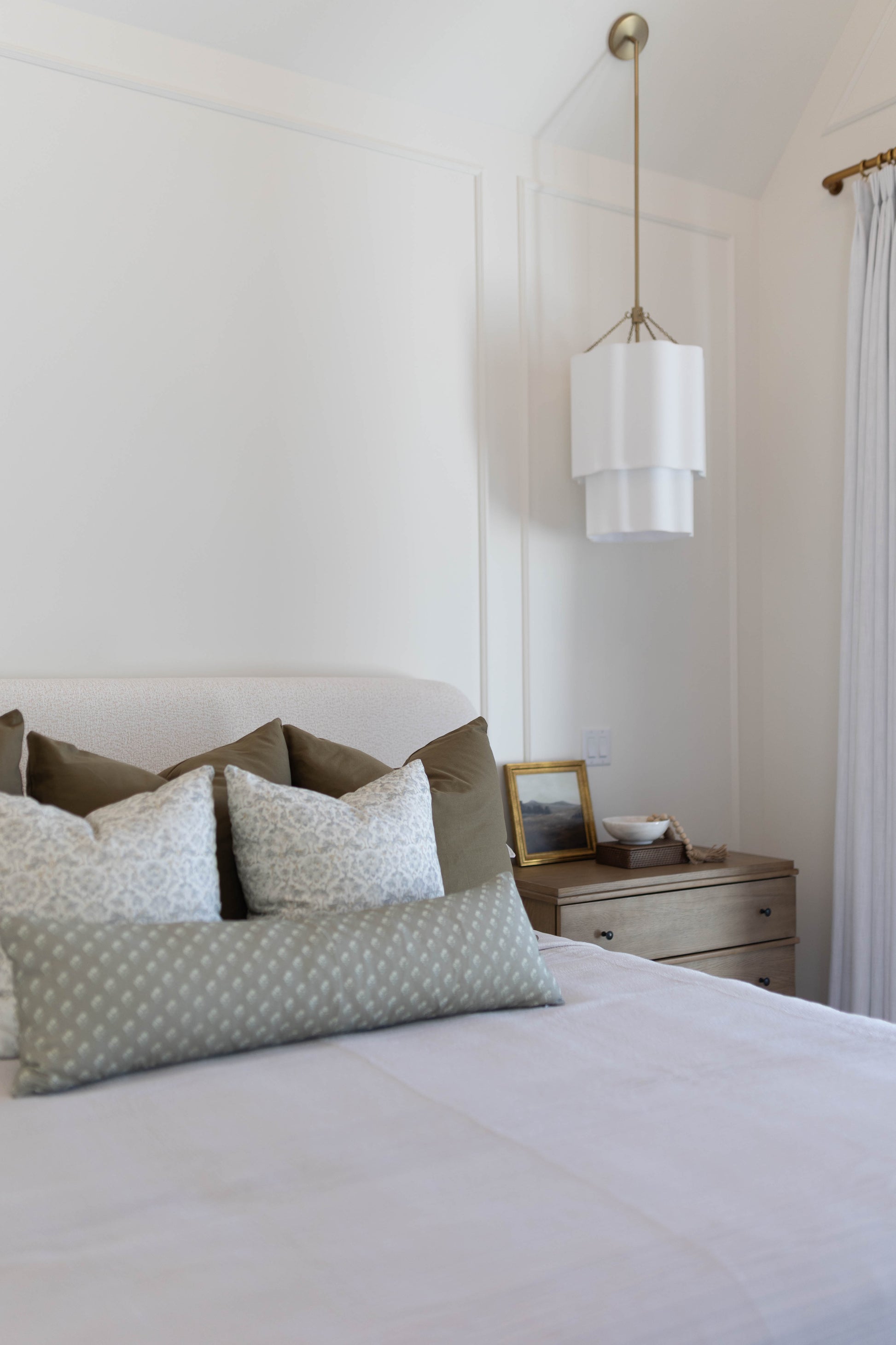King bed with light blue patterned pillow covers and olive green pillows arranged against upholstered headboard.