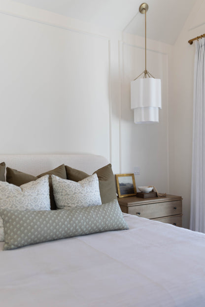 King bed with light blue patterned pillow covers and olive green pillows arranged against upholstered headboard.