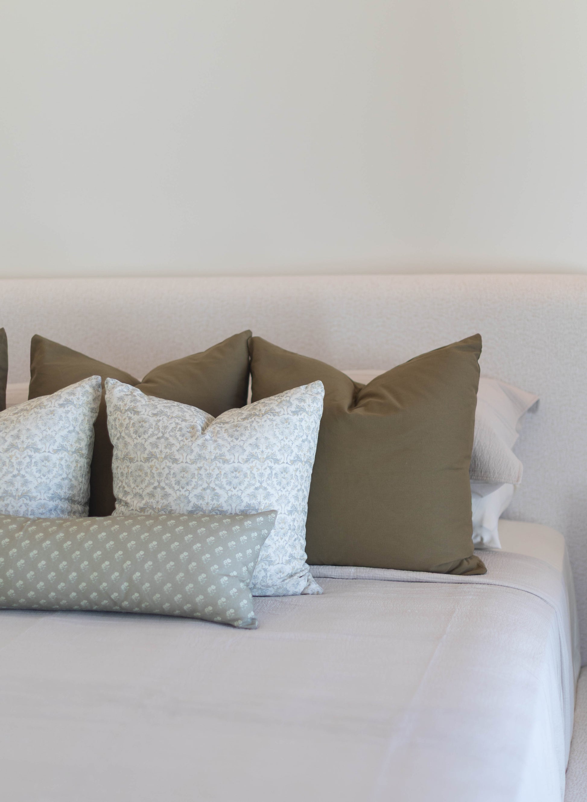 King bed pillow covers in sage green and cream patterned fabrics arranged on a light bedding set.