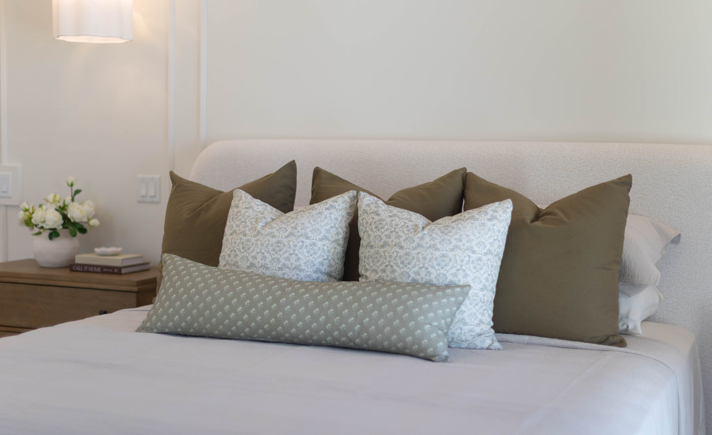King bed with five pillow covers in olive green and light blue patterned designs arranged against headboard.