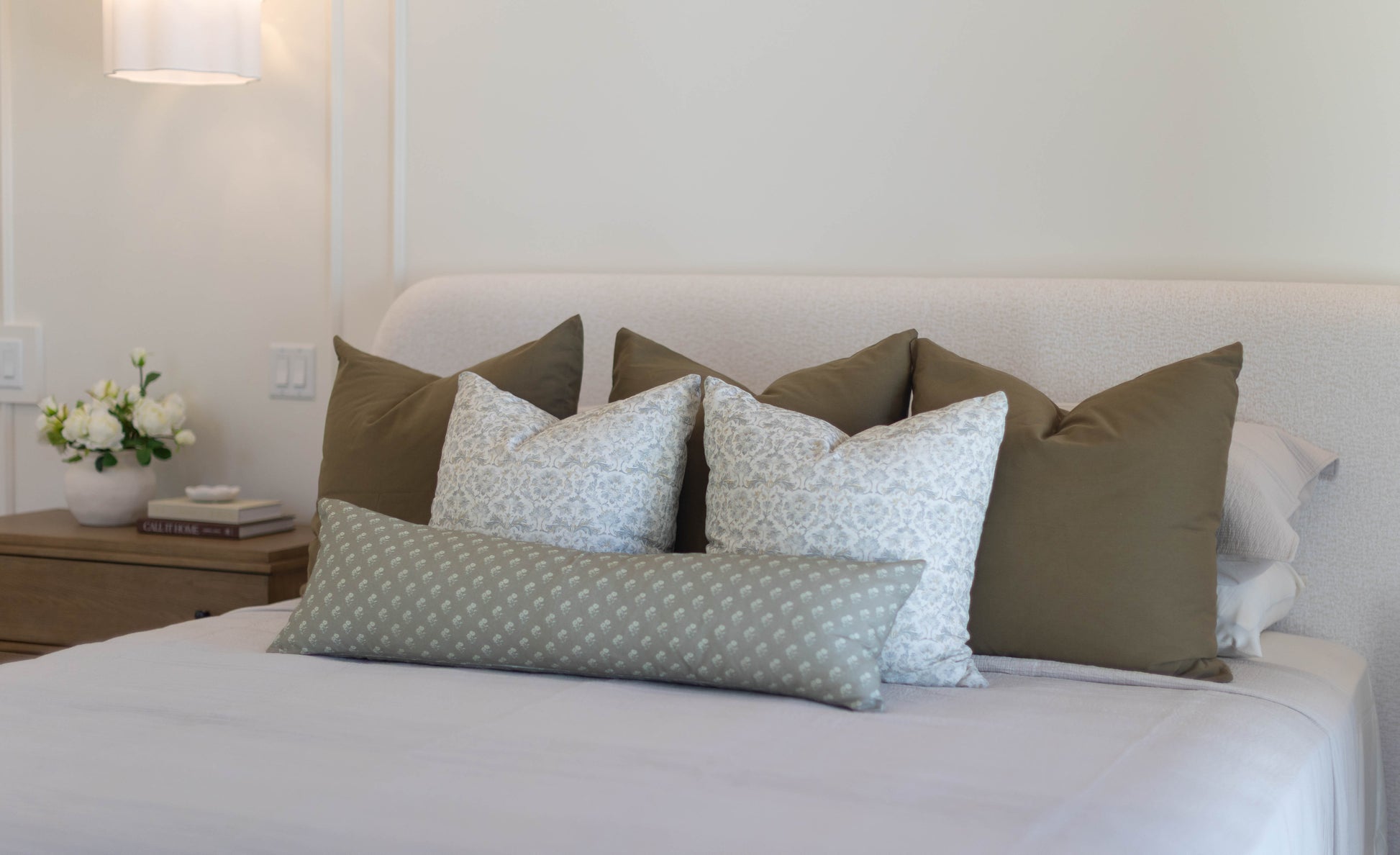 King bed with five pillow covers in olive green and light blue patterned designs arranged against headboard.