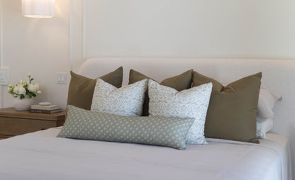 King bed with five pillow covers in olive green and light blue patterned designs arranged against headboard.