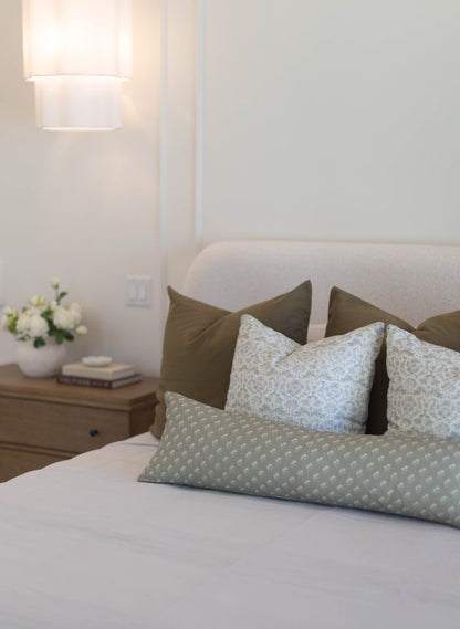 King bed with sage green and blue patterned pillow covers arranged against matching solid pillows.