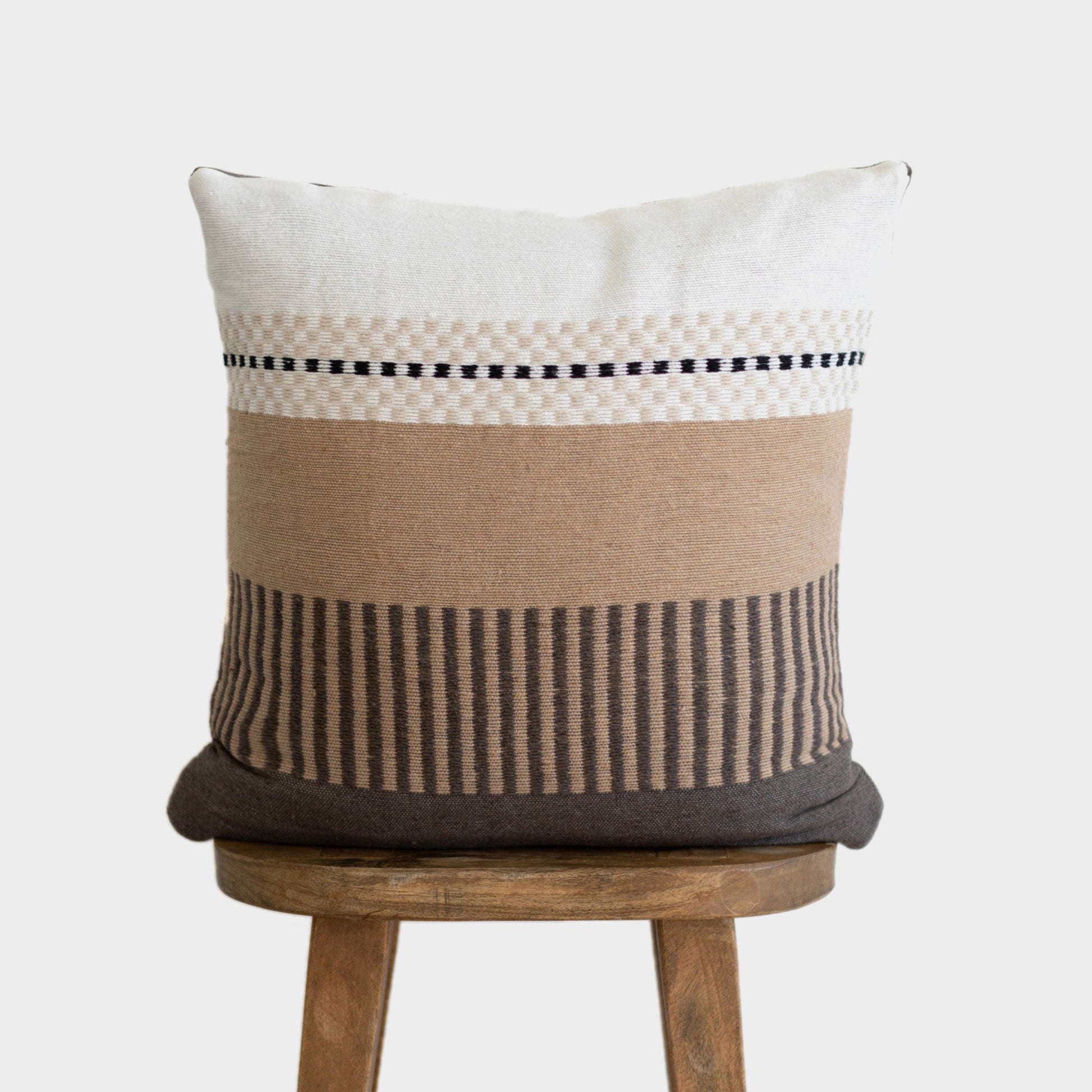 Cream, tan, and charcoal striped 22-inch square pillow with geometric patterns displayed on wooden stool.
