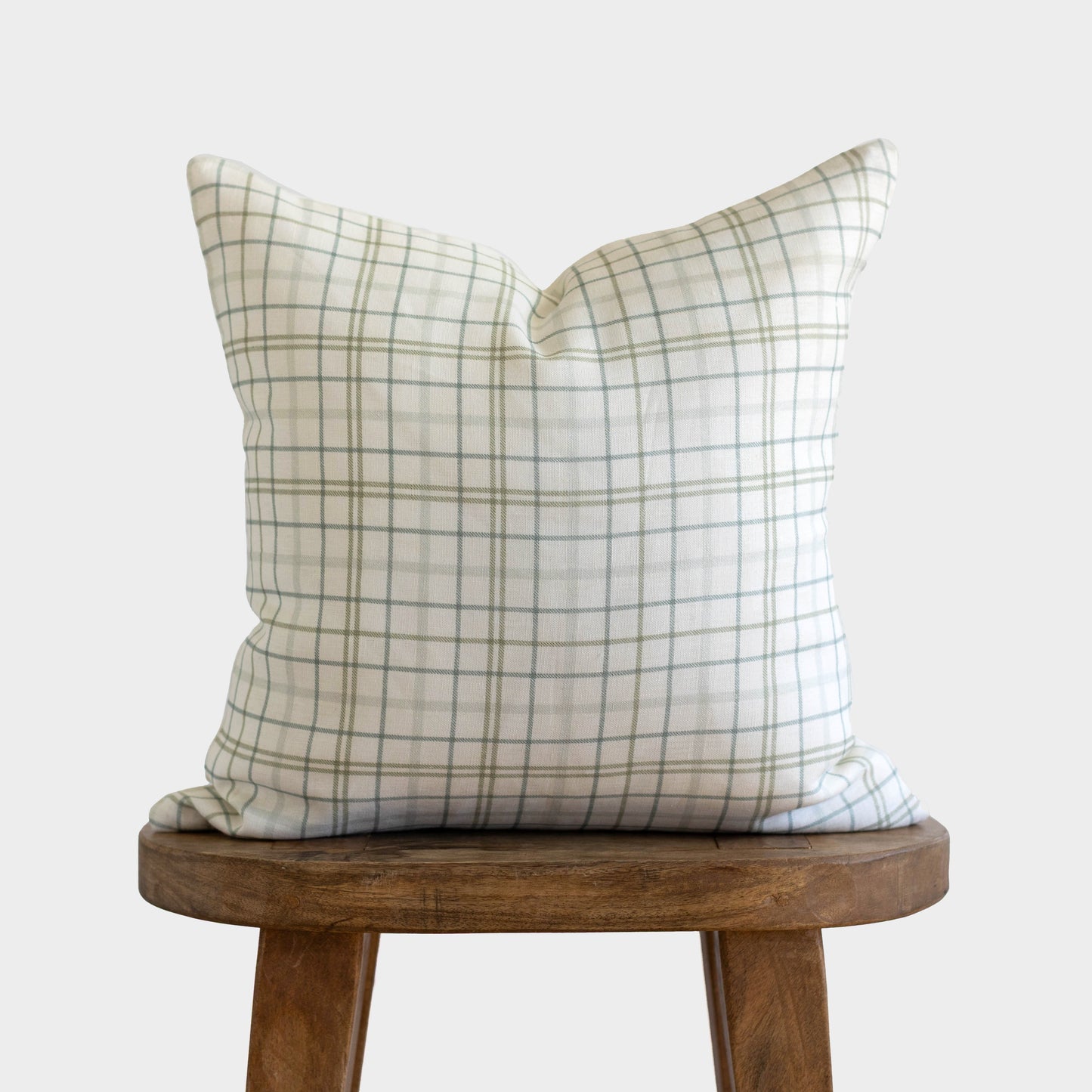 Beige and gray plaid linen pillow on wooden stool against white background.