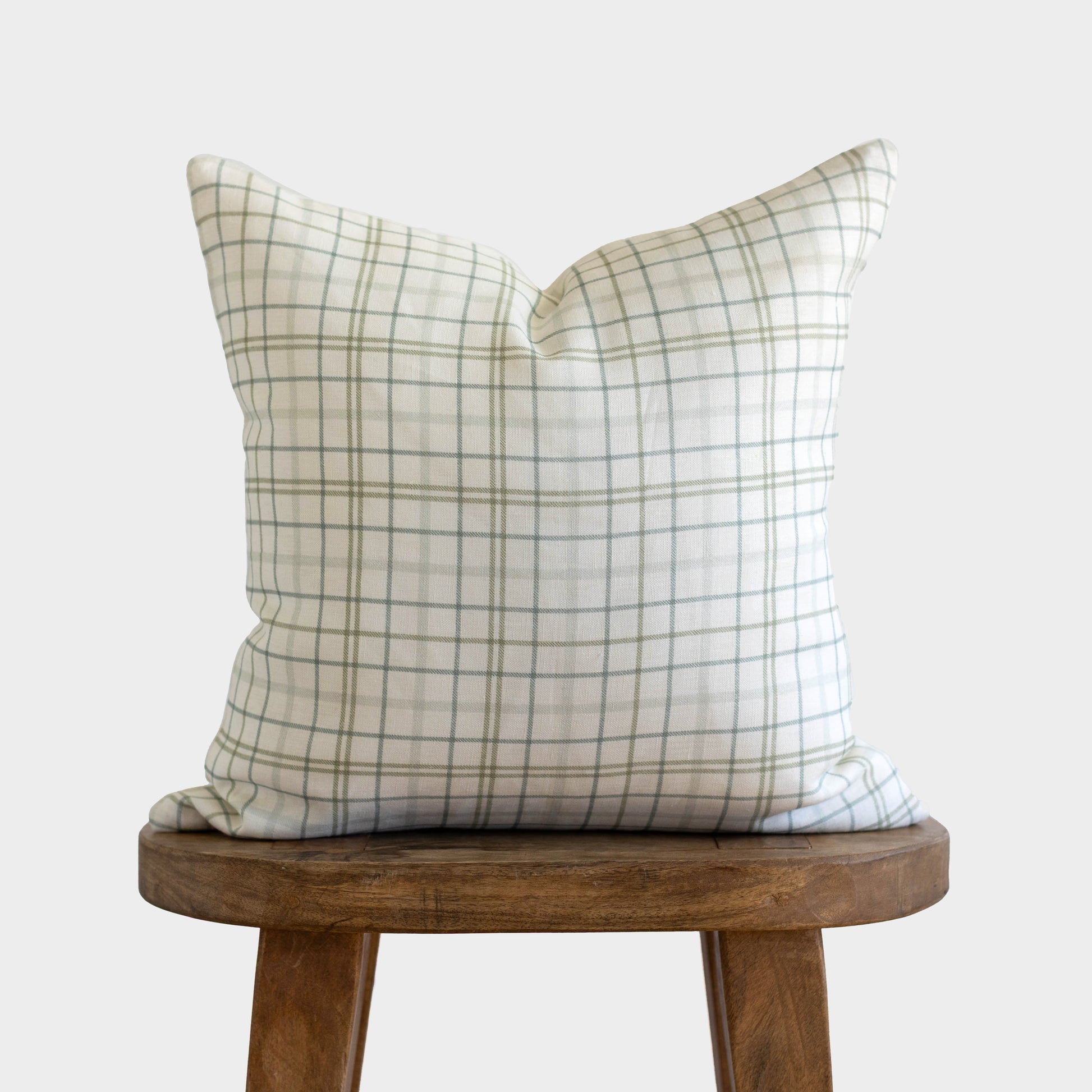 Beige and gray plaid linen pillow on wooden stool against white background.