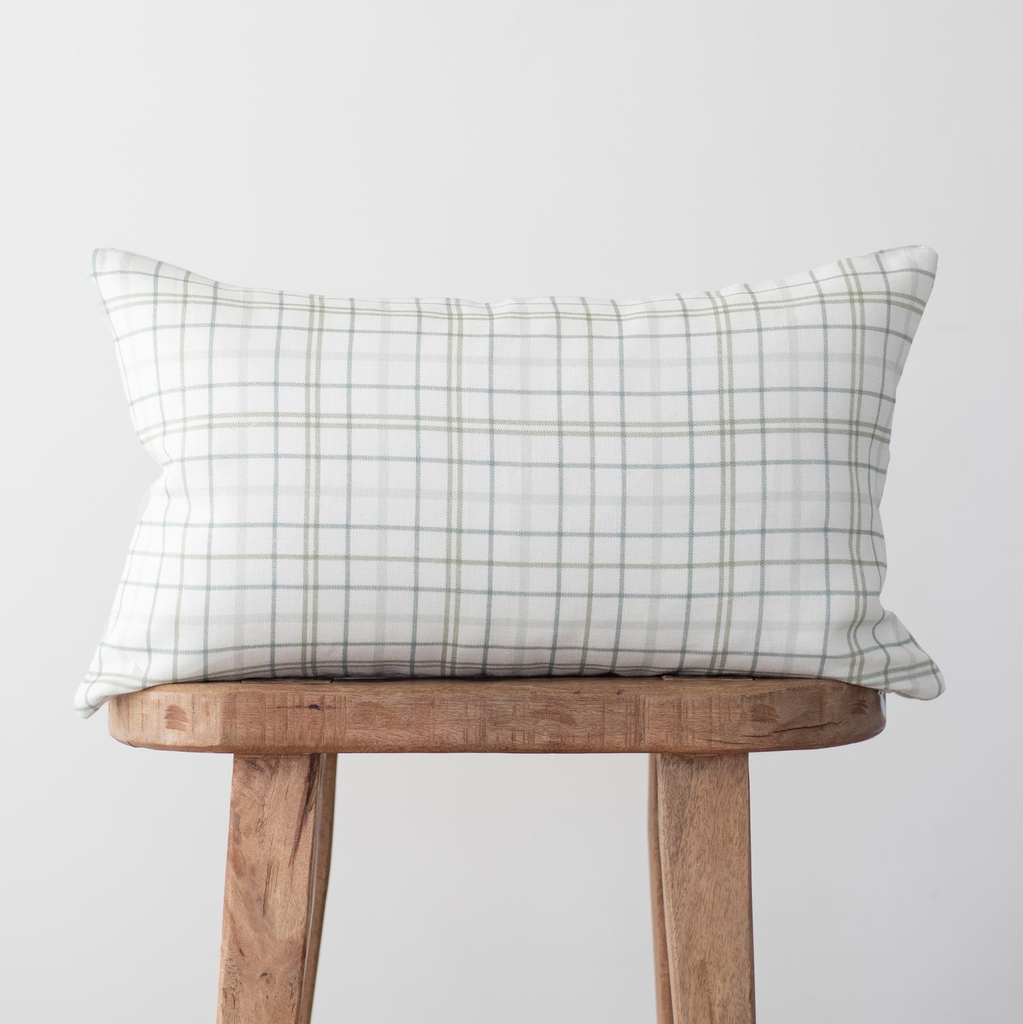 Rectangular linen pillow with gray and white plaid pattern displayed on wooden stool.