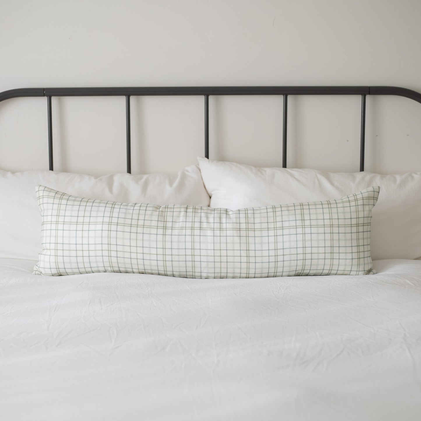 Lumbar linen pillow with green and white grid pattern on a bed with metal headboard.