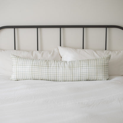 Lumbar linen pillow with green and white grid pattern on a bed with metal headboard.