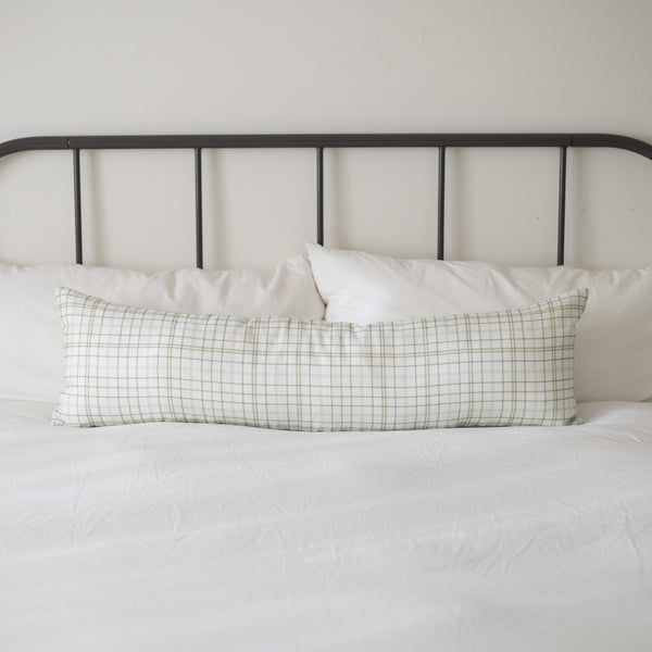 Lumbar linen pillow with green and white grid pattern on a bed with metal headboard.