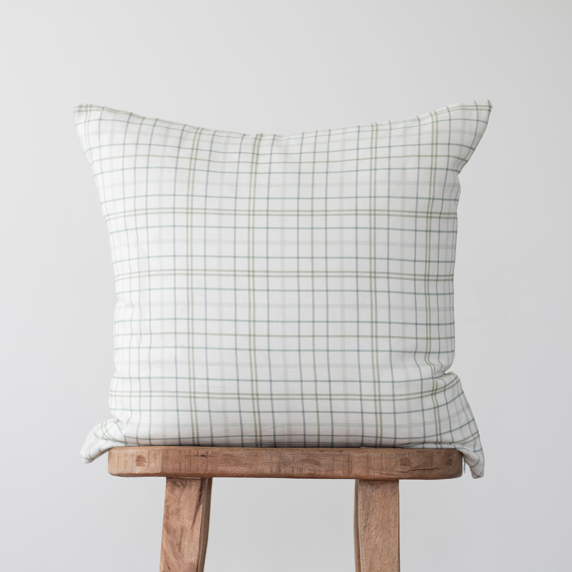 White linen pillow with gray plaid pattern displayed on wooden chair.