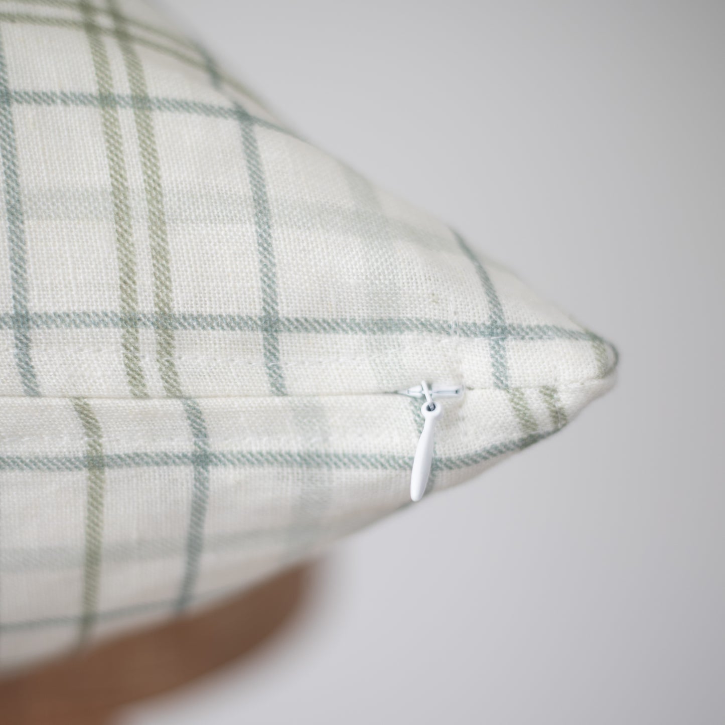 Cream linen pillow with sage green plaid pattern and white zipper closure.