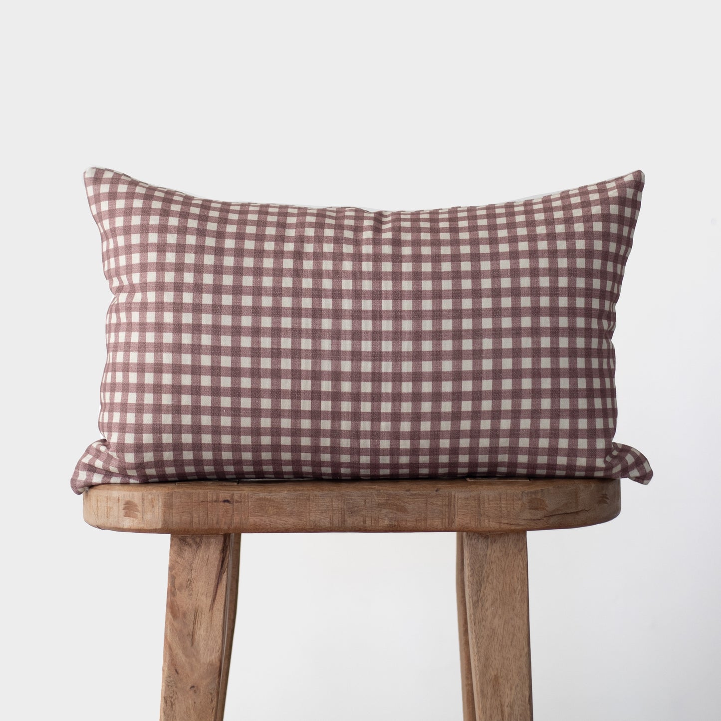 Rose and white gingham check pillow on wooden stool.