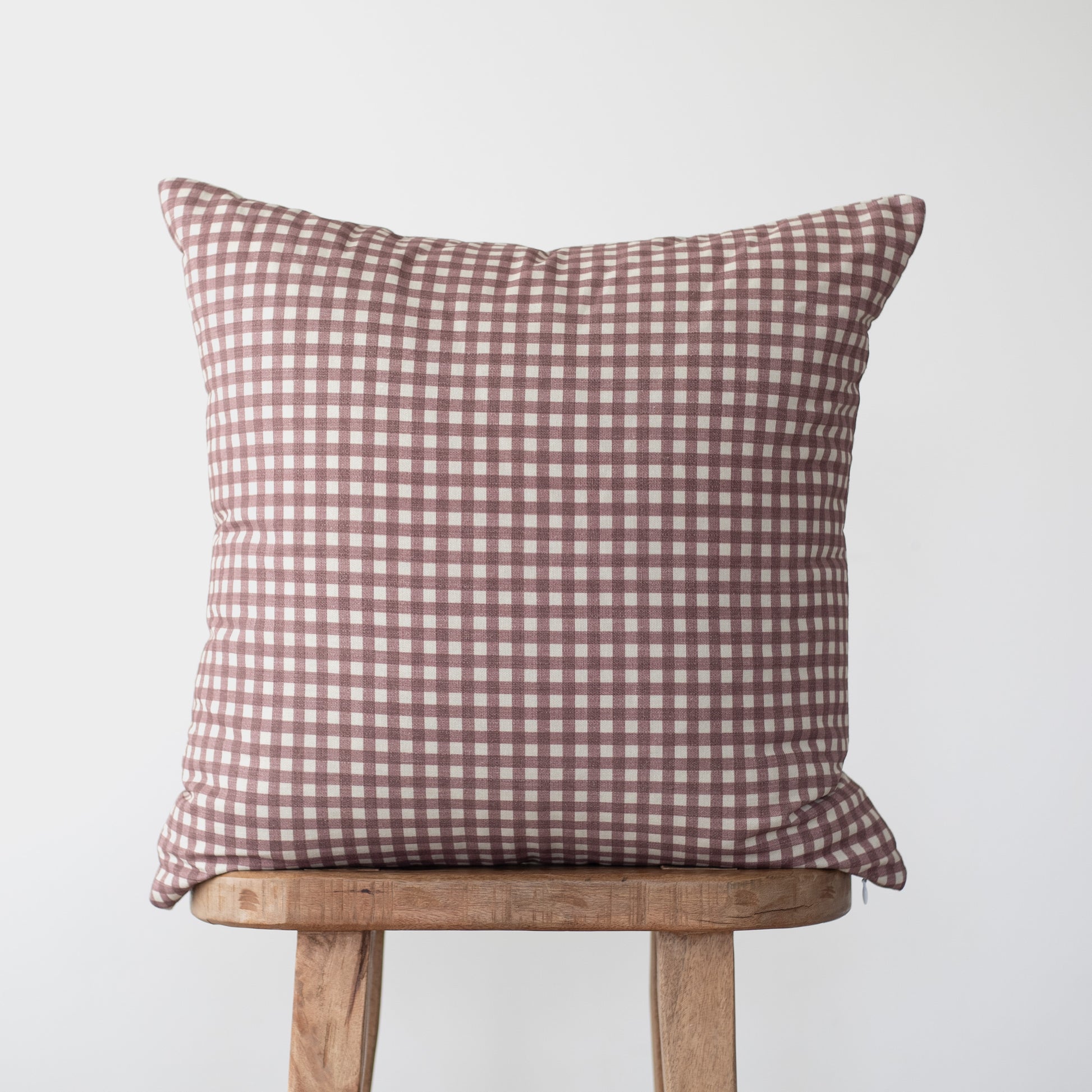 Rose and white gingham checkered pillow on wooden stool.