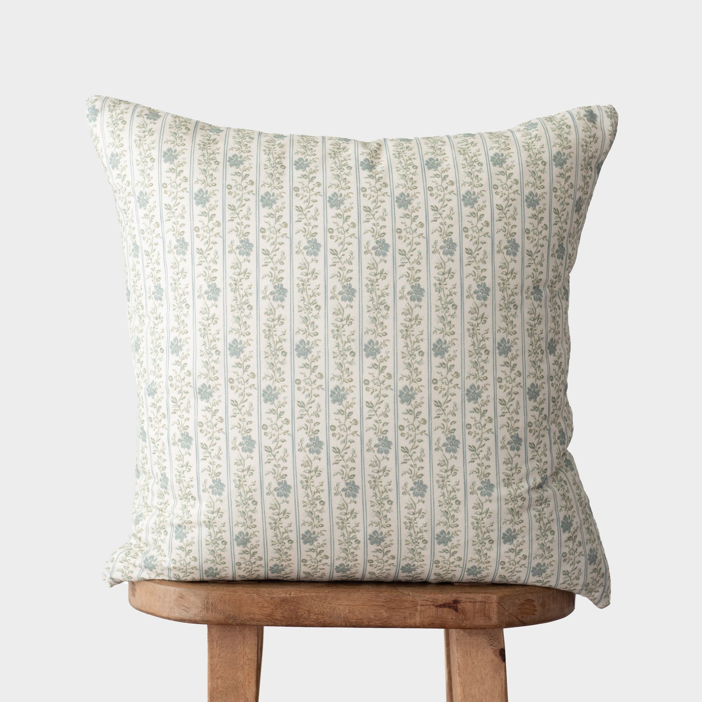 Cream pillow with vertical green stripes and small floral pattern, displayed on wooden stool.
