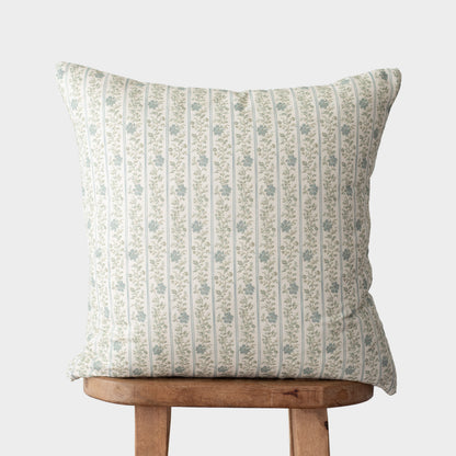 Cream pillow with vertical green stripes and small floral pattern, displayed on wooden stool.