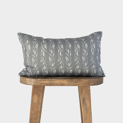Rectangular lumbar pillow with sage green fabric featuring white leaf pattern, displayed on wooden stool.