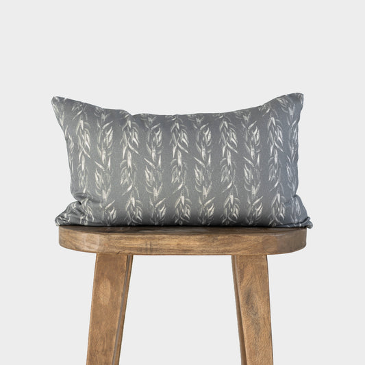 Rectangular lumbar pillow with sage green fabric featuring white leaf pattern, displayed on wooden stool.