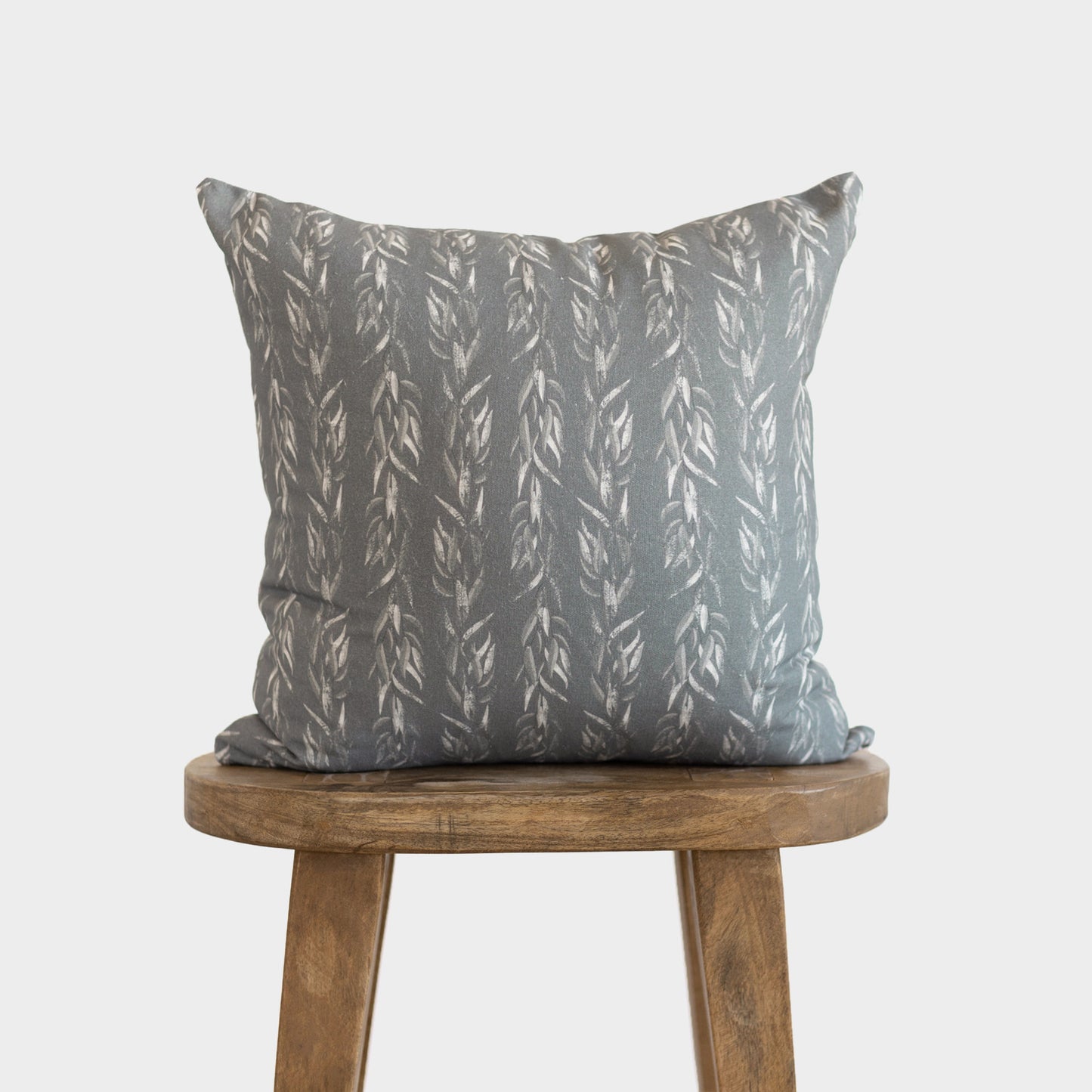 Gray throw pillow with vertical sage leaf pattern in cream, displayed on wooden stool.
