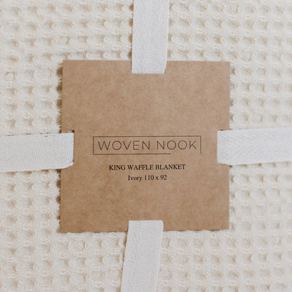 Ivory waffle textured blanket with white fabric straps and kraft paper product label.