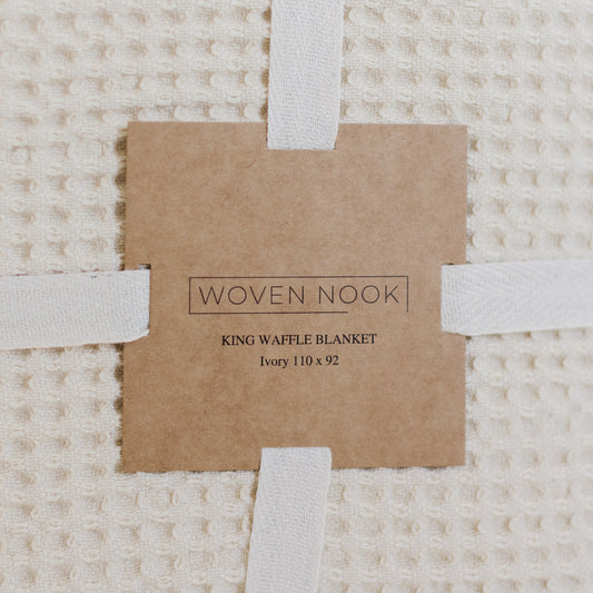 Ivory waffle textured blanket with white fabric straps and kraft paper product label.