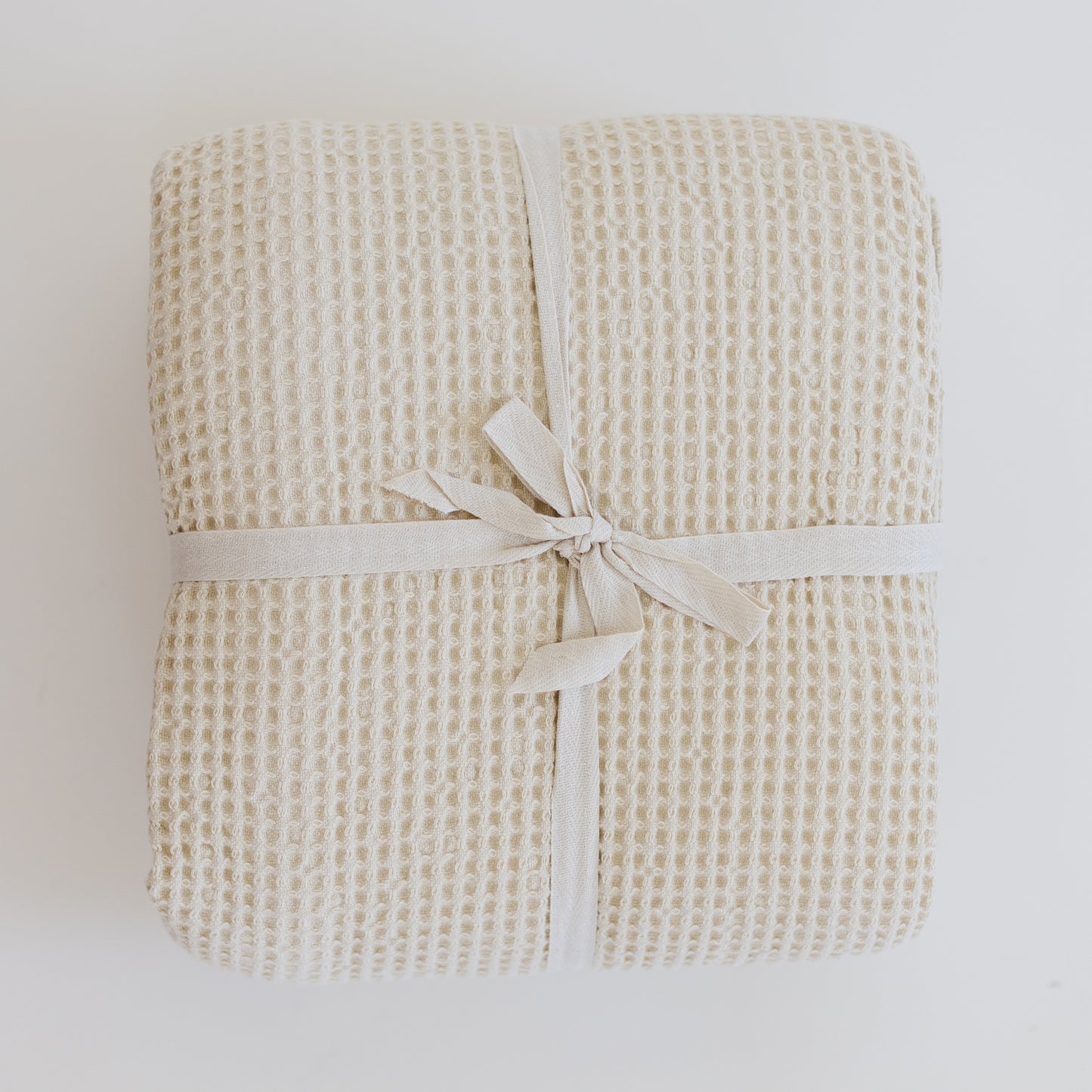 Ivory waffle-textured blanket folded and tied with a cream-colored ribbon bow.